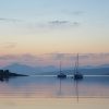 a calm Loch Ness as two yachts sit in front of the sunset coloured sky
