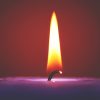 A still candle flame lit on a purple candle, without a draught hitting it. A small wick may determine why some candles burn faster than others