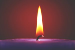 A still candle flame lit on a purple candle, without a draught hitting it. A small wick may determine why some candles burn faster than others