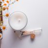 a view of a white candle from above, which sits next to an open jar of matches with some daisy entering the image from the right