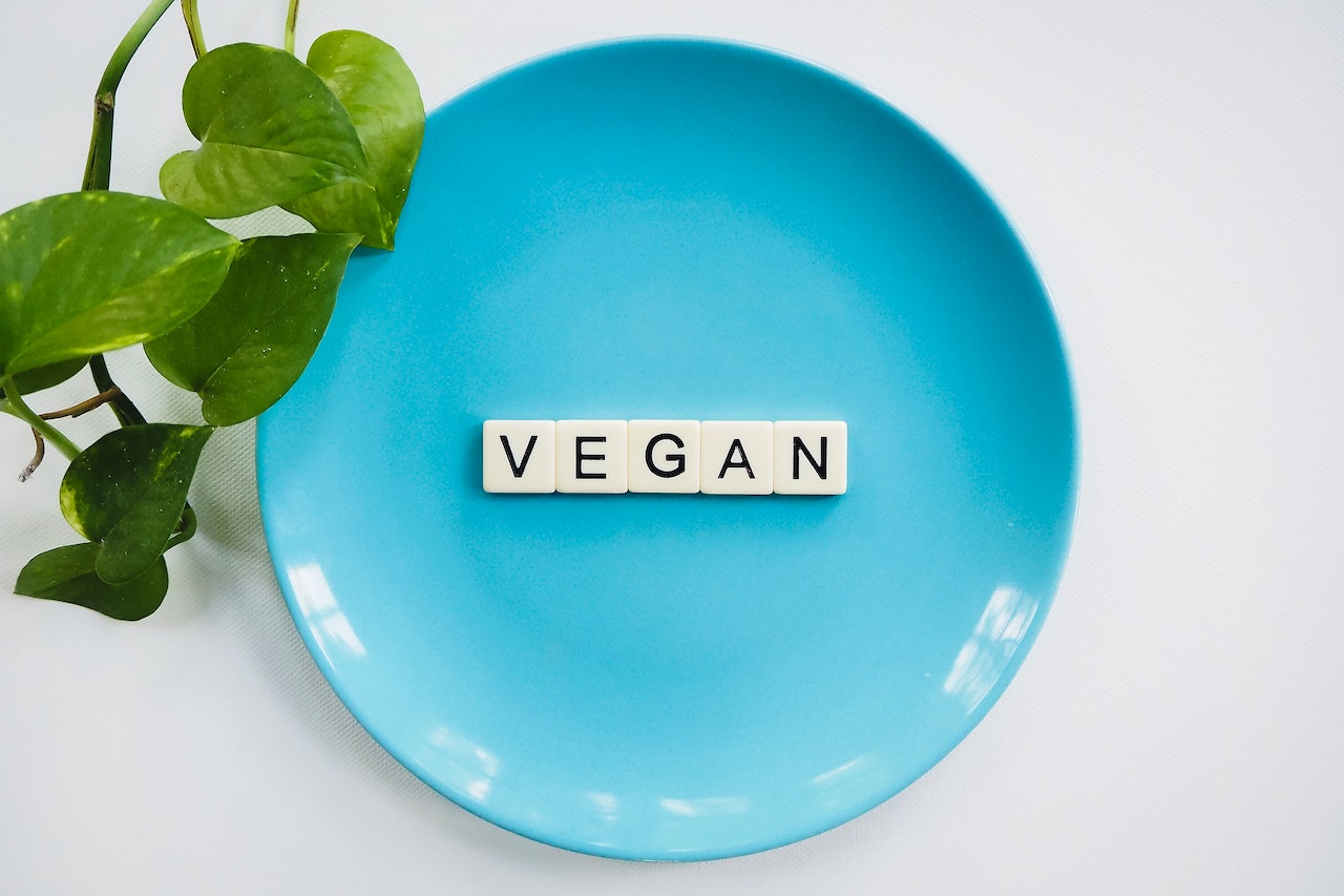 a blue plate with scrabble letters spelling out vegan, with a green leaf entering the image from the right. Used for a blog about vegan candle