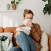 Women sits on a couch in a bright room blowing her nose after being affected from candle allergies