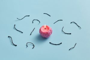 A small pink candle sits in the middle of the image with parts of used candle wicks laying surrounding the candle. Important to know what is best to choosing your wick