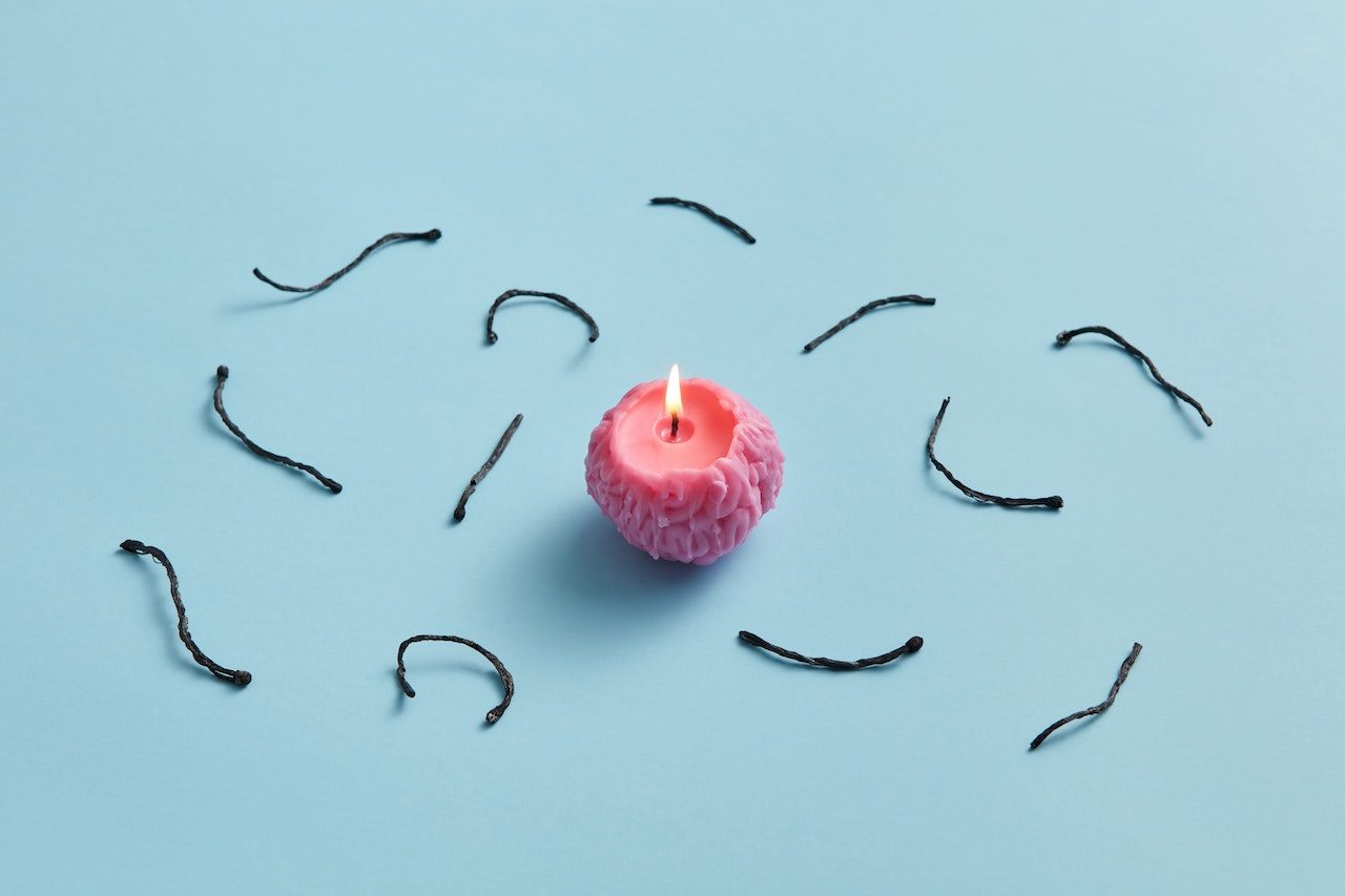 A small pink candle sits in the middle of the image with parts of used candle wicks laying surrounding the candle. Important to know what is best to choosing your wick