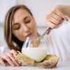 A woman sticks a pair of scissors inside a glass candle jar showing how to trim a candle wick. The wick is a wooden wick in soy wax