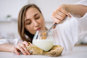 A woman sticks a pair of scissors inside a glass candle jar showing how to trim a candle wick. The wick is a wooden wick in soy wax