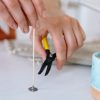 A cotton candle wick that has not yet been put into a candle is about to be trimmed with a pair of clippers to the correct wick length