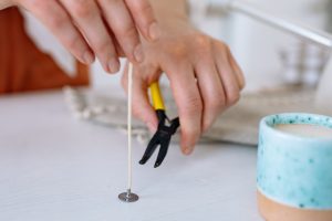 A cotton candle wick that has not yet been put into a candle is about to be trimmed with a pair of clippers to the correct wick length
