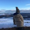 Boy stands at the viewpoint up Cairngorm mountain in the snow-covered hills, clear blue sky in the Highlands of Scotland