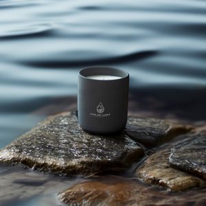 A grey candle container/glass/ jar sits outdoors on wet rocky ground on the shorelines of the Isle of Skye. This is a candle filled with natural soy and coconut wax from a Scottish candle company named 'Highland Candle Company', is their candle named 'Skye', after the Scottish island.