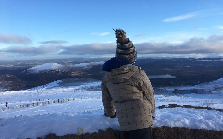 Boy stands at the viewpoint up Cairngorm mountain in the snow-covered hills, clear blue sky in the Highlands of Scotland