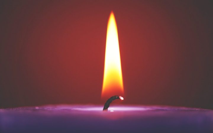 A still candle flame lit on a purple candle, without a draught hitting it. A small wick may determine why some candles burn faster than others