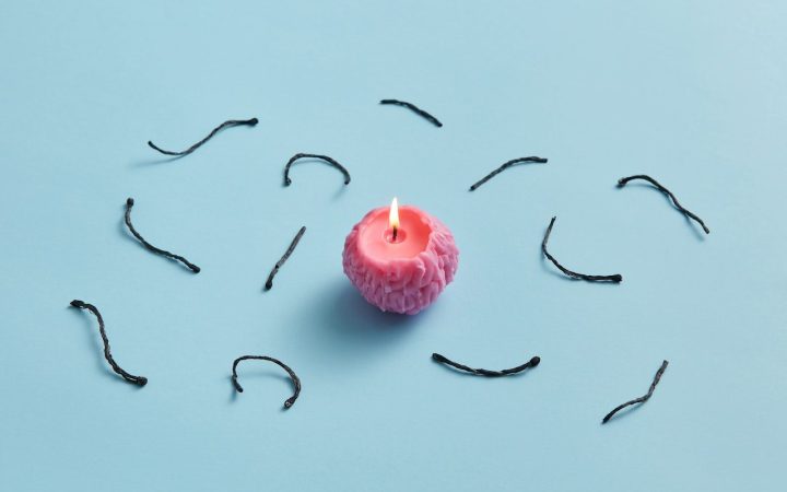 A small pink candle sits in the middle of the image with parts of used candle wicks laying surrounding the candle. Important to know what is best to choosing your wick