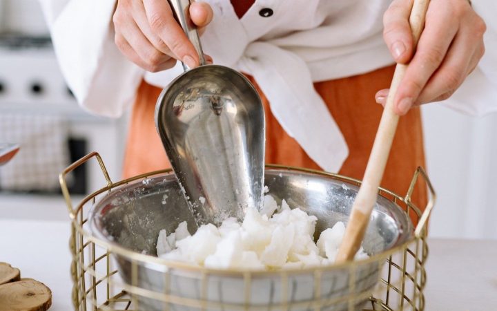 person mixes Soy candle wax in a metal bowl with a wooden spoon