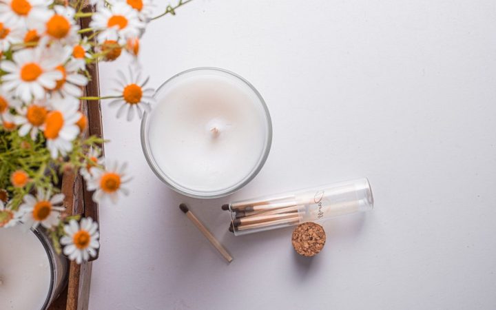 a view of a white candle from above, which sits next to an open jar of matches with some daisy entering the image from the right