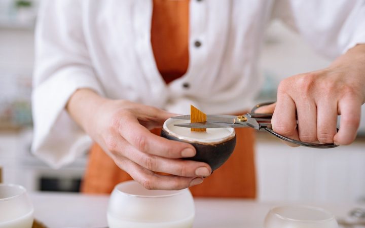 Person trimming candle wick with scissors for proper burning and clean environment. The soy and coconut candle will now be left to cure