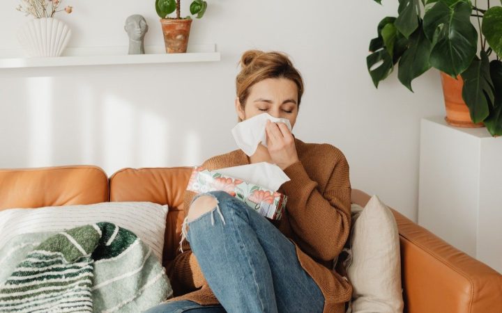 Women sits on a couch in a bright room blowing her nose after being affected from candle allergies