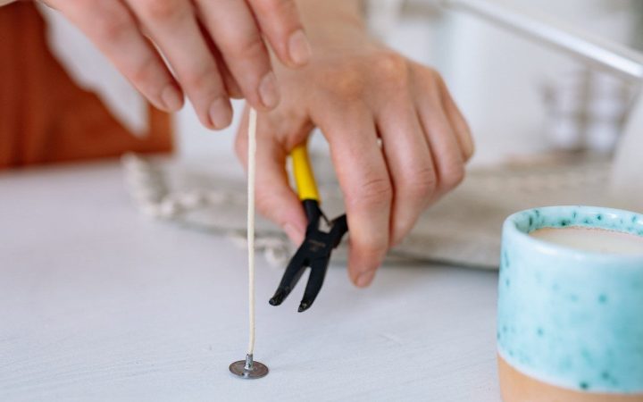 A cotton candle wick that has not yet been put into a candle is about to be trimmed with a pair of clippers to the correct wick length