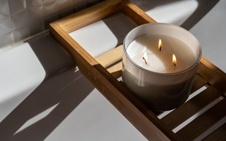 candle with 3 wicks sitting on a shelf over a bathtub
