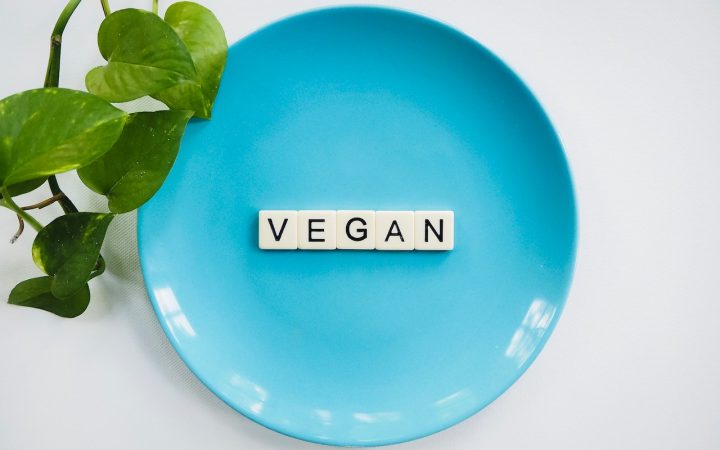 a blue plate with scrabble letters spelling out vegan, with a green leaf entering the image from the right. Used for a blog about vegan candle