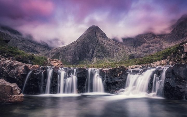 a sunset pink sky above a small waterfall and mountain at the fairy pools on the isle of skye