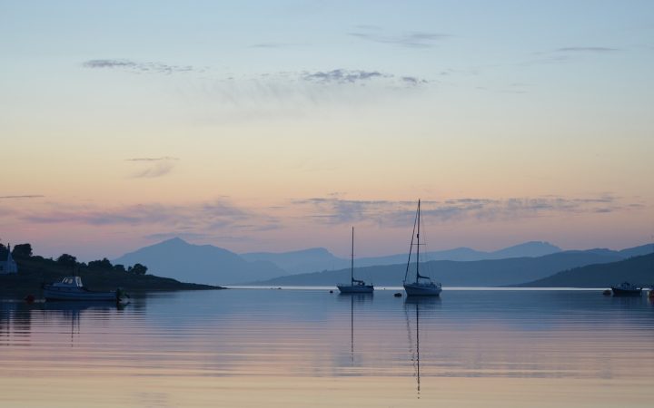 a calm Loch Ness as two yachts sit in front of the sunset coloured sky